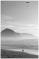 Motorized paraglider, women walking dog, and Morro Rock seen from Cayucos Beach. Morro Bay, USA (black and white)