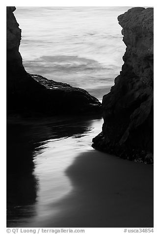 Reflection on wet sand through rock opening, Natural Bridges State Park, dusk. Santa Cruz, California, USA