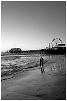 Couple standing on the beach at sunset, with pier and Ferris Wheel behind. Santa Monica, Los Angeles, California, USA ( black and white)