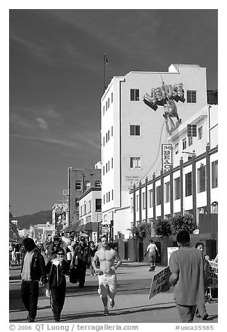 Jogger in the crowd of Ocean Front Walk, with a Venice Mural behind. Venice, Los Angeles, California, USA (black and white)