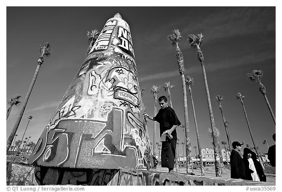 Man painting inscriptions on a graffiti-decorated tower. Venice, Los Angeles, California, USA (black and white)