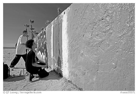 Young men creating graffiti art on a wall on the beach. Venice, Los Angeles, California, USA (black and white)