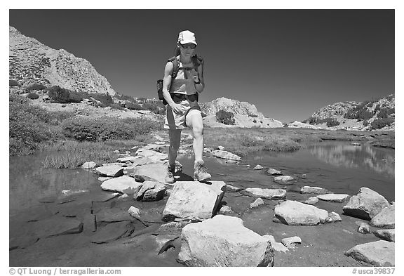 Woman crossing stream on rocks, John Muir Wilderness. California, USA