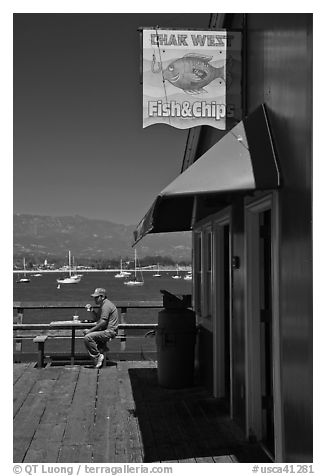 Man eating on wharf next to Fish and Chips restaurant. Santa Barbara, California, USA (black and white)