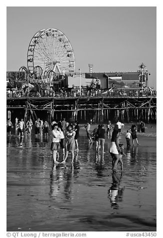 Pier and beachgoers reflected in wet sand, late afternoon. Santa Monica, Los Angeles, California, USA (black and white)