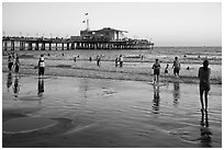 Beachgoers near Santa Monica Pier reflected in wet sand, sunset. Santa Monica, Los Angeles, California, USA ( black and white)