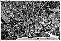 Man sitting in car, mural, and tree, Mission District. San Francisco, California, USA (black and white)