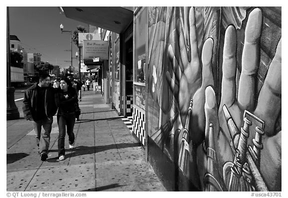 Couple walks past mural on Mission street, Mission District. San Francisco, California, USA (black and white)