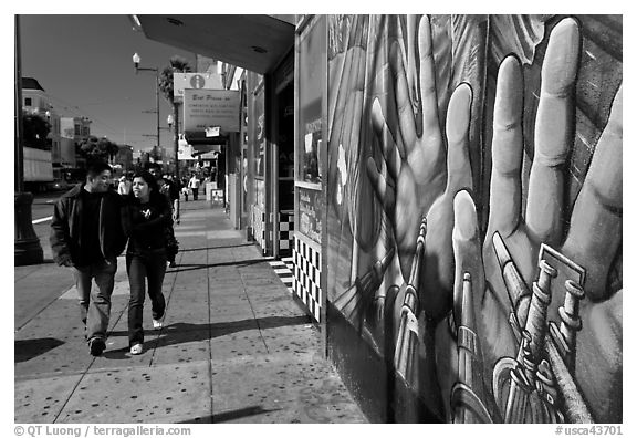 Couple walks past mural on Mission street, Mission District. San Francisco, California, USA