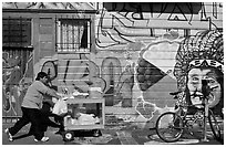 Man pushes vending cart pass mural and bicycle, Mission District. San Francisco, California, USA (black and white)