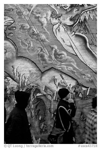 Men in dark jackets walk past mural, Mission District. San Francisco, California, USA (black and white)