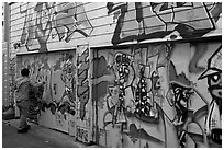 Man hanging poster on painted garage door, Mission District. San Francisco, California, USA (black and white)