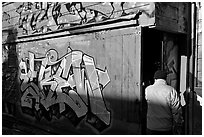 Man opening door of painted garage, Mission District. San Francisco, California, USA ( black and white)