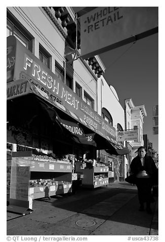 Woman walks past vegetable store, Mission Street, Mission District. San Francisco, California, USA (black and white)