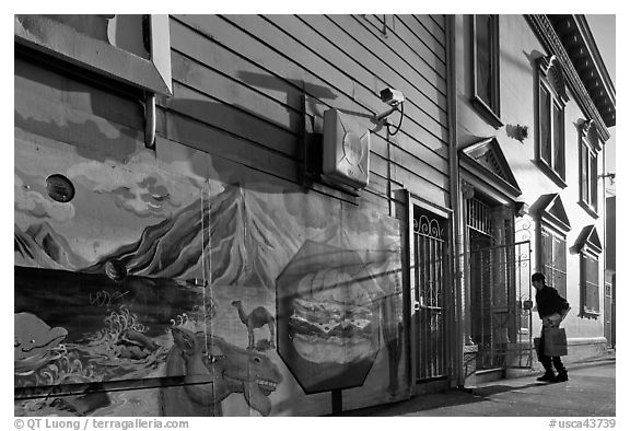 Mural and man entering house with grocery bags, Mission District. San Francisco, California, USA (black and white)