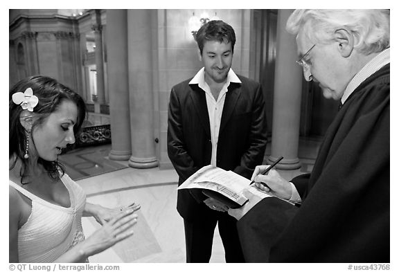 Officiant signing marriage papers as bride looks at ring on finger, City Hall. San Francisco, California, USA (black and white)