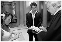 Officiant signing marriage papers as bride looks at ring on finger, City Hall. San Francisco, California, USA (black and white)