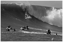 Surfer down huge wall of water observed from jet skis. Half Moon Bay, California, USA (black and white)