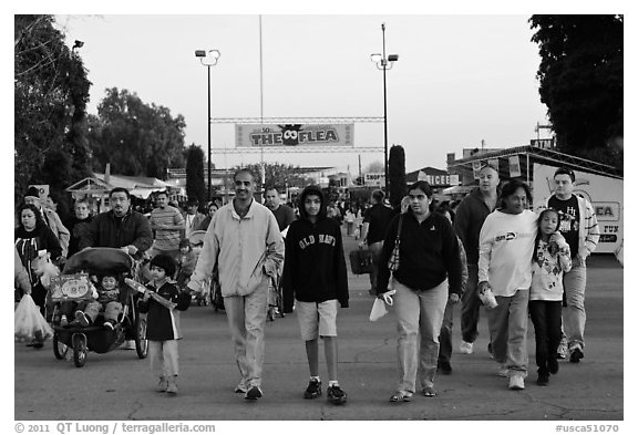 Families walking with entrance sign behind, San Jose Flee Market. San Jose, California, USA (black and white)