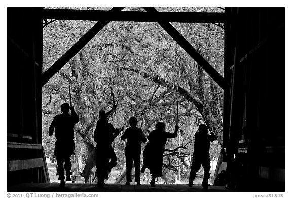 Silhouettes of dancers with sticks inside covered bridge, Felton. California, USA (black and white)