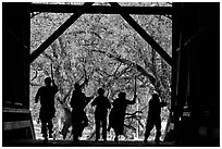 Silhouettes of dancers with sticks inside covered bridge, Felton. California, USA (black and white)