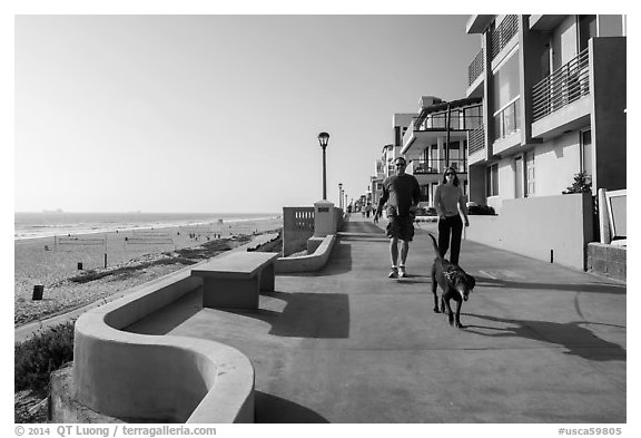 Couple walking dog on beachfront promenade, Manhattan Beach. Los Angeles, California, USA (black and white)