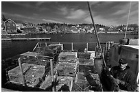 Lobsterman in boat with traps, and village in background. Stonington, Maine, USA (black and white)