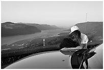 Couple embracing on car hood, with view of mouth of river gorge. Columbia River Gorge, Oregon, USA (black and white)