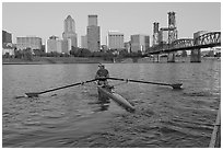 Woman rowing on racing shell and city skyline at sunrise. Portland, Oregon, USA (black and white)