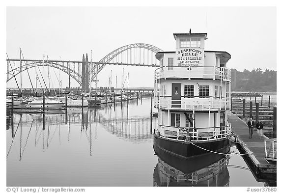 Couple walking on deck next to floating Bed and Breakfast. Newport, Oregon, USA (black and white)