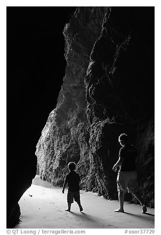 Father and son walking towards the light in sea cave. Bandon, Oregon, USA (black and white)