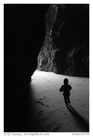 Infant walking towards the light in sea cave. Bandon, Oregon, USA (black and white)