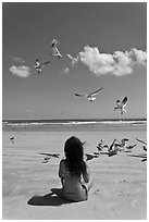 Girl sitting on beach with birds flying, Jetty Park. Cape Canaveral, Florida, USA (black and white)