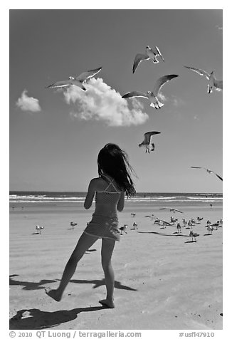 Girl playing with seabirds, Jetty Park beach. Cape Canaveral, Florida, USA (black and white)