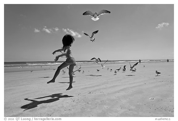 Girl jumping on beach with seagulls flying, Jetty Park. Cape Canaveral, Florida, USA (black and white)