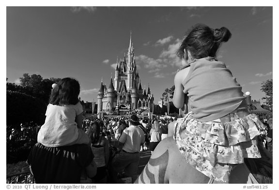 Toddlers sit on parent shoulders druing stage show. Orlando, Florida, USA (black and white)