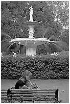 Woman sitting on bench with book in front of Forsyth Park Fountain. Savannah, Georgia, USA (black and white)