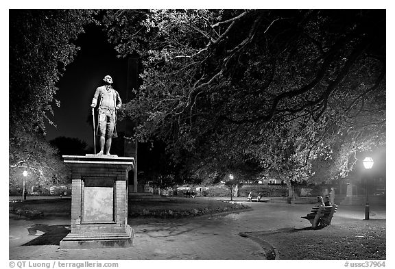 Park with statue and couples sitting on public benches at night. Charleston, South Carolina, USA (black and white)