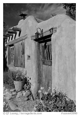 Flowers, adobe wall, and weathered door. Santa Fe, New Mexico, USA (black and white)