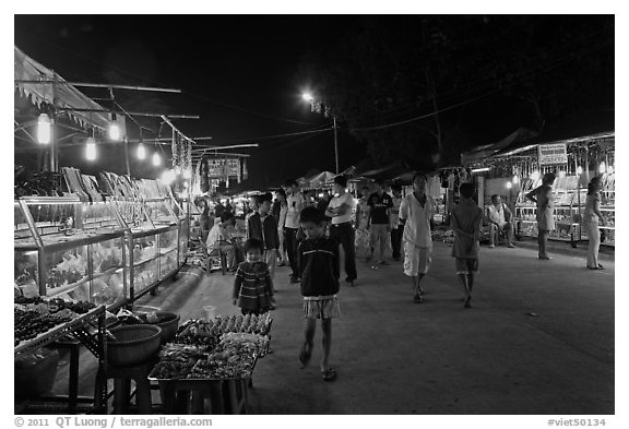 Shoppers walk past craft booth at night market. Phu Quoc Island, Vietnam