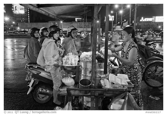 Women riding motorbikes buy sweet rice. Ho Chi Minh City, Vietnam (black and white)