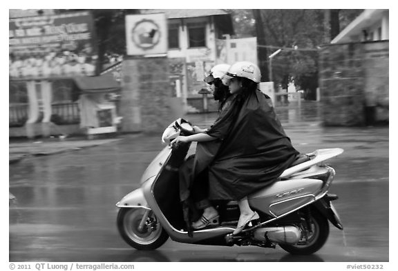 Women ride motorcycle in the rain. Ho Chi Minh City, Vietnam (black and white)