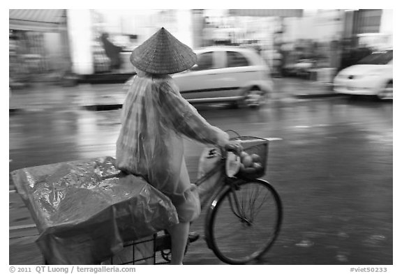 Woman rides bicycle in the rain. Ho Chi Minh City, Vietnam (black and white)