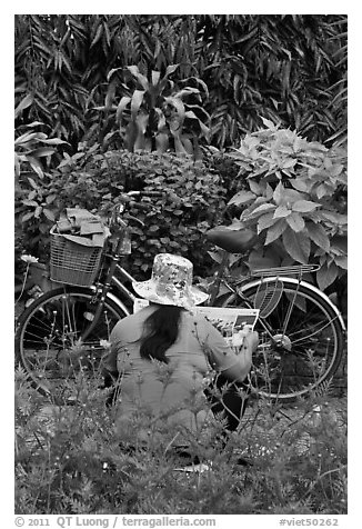 Woman reading newspaper next to bicycle in park. Ho Chi Minh City, Vietnam