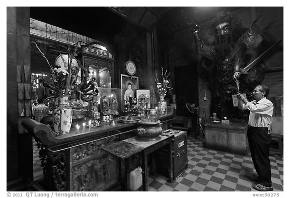 Man in prayer, with fierce statue of general behind, Jade Emperor Pagoda, district 3. Ho Chi Minh City, Vietnam (black and white)