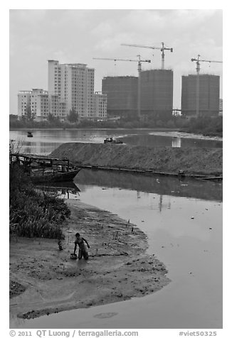 Man wading in mud, with background of towers in construction, Phu My Hung, district 7. Ho Chi Minh City, Vietnam