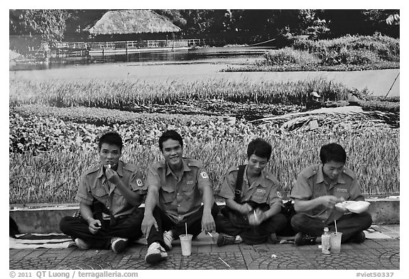 Uniformed students eating in front of backdrop depicting rural landscape. Ho Chi Minh City, Vietnam