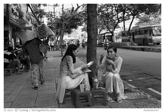 Women elegantly dressed in ao dai eating on the street. Ho Chi Minh City, Vietnam