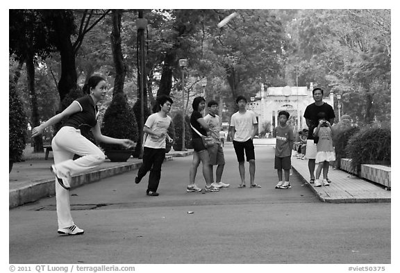Young woman playing footbag as audience watches, Cong Vien Van Hoa Park. Ho Chi Minh City, Vietnam (black and white)