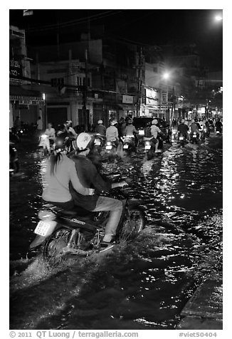 Couple riding motorcycle on flooded street at night. Ho Chi Minh City, Vietnam (black and white)